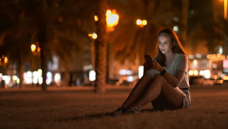 Young-woman-tourist-travels-through-the-night-megalopolis-and-writes-text-messages-on-social-networks-about-the-journey-holds-the-phone-in-her-hands-and-looks-at-the-screen-of-the-gadget